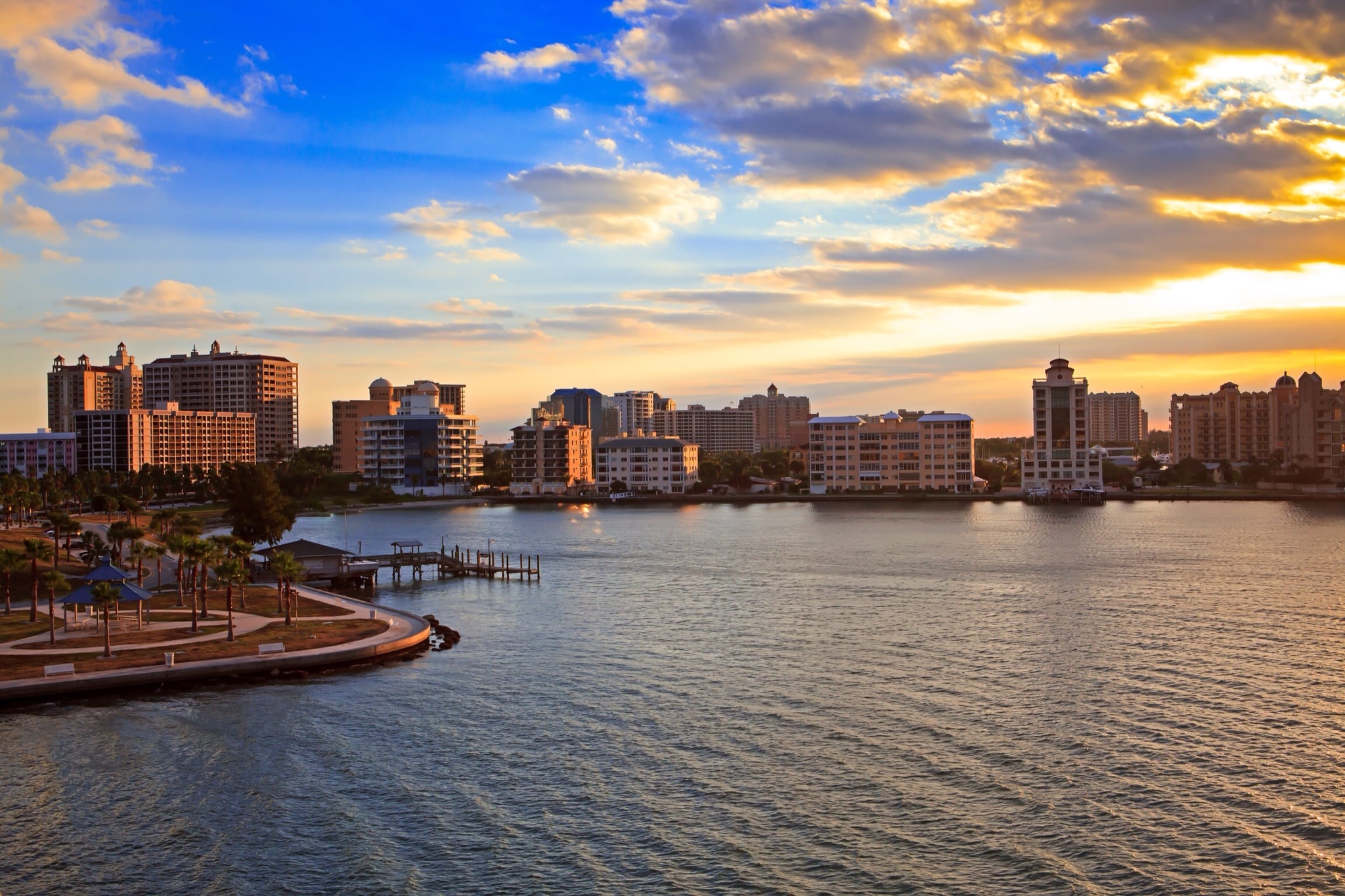 Waterfront city skyline at sunset with mid-rise buildings and calm water, orange and blue tones